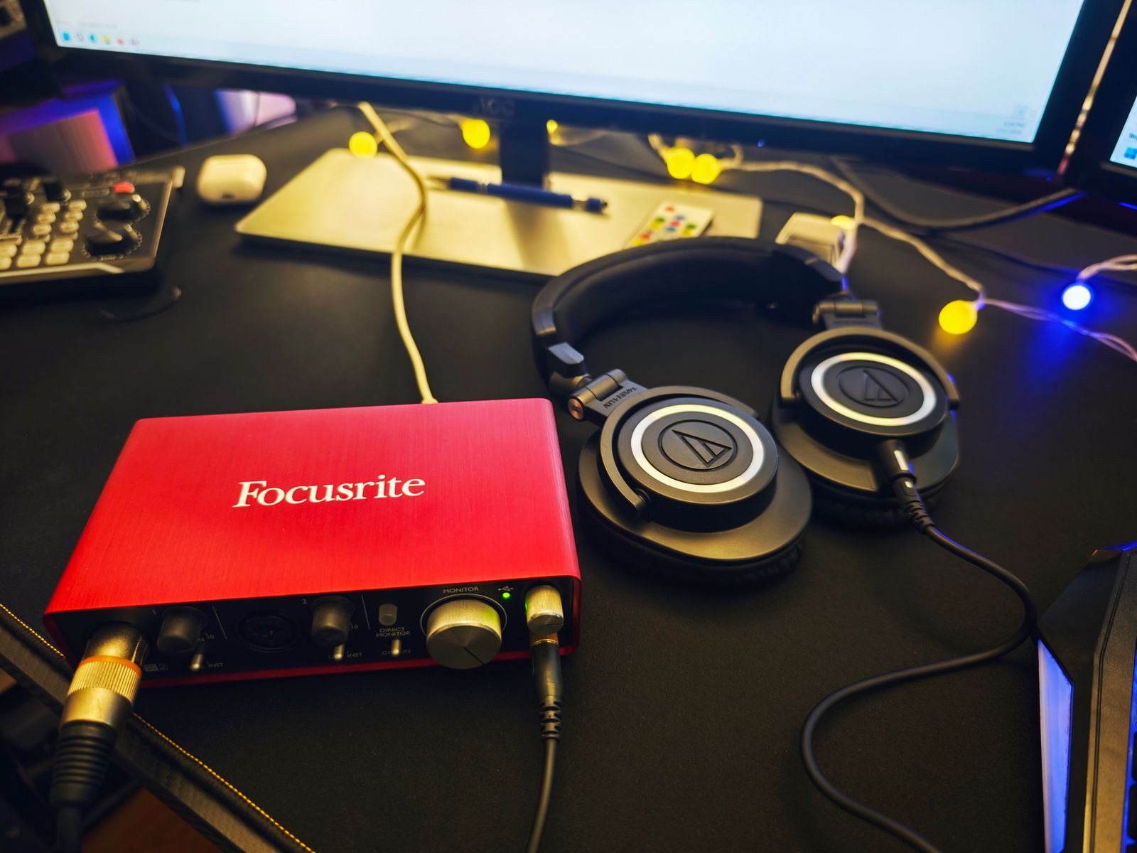 A red audio interface with front-panel inputs beside headphones on a desk