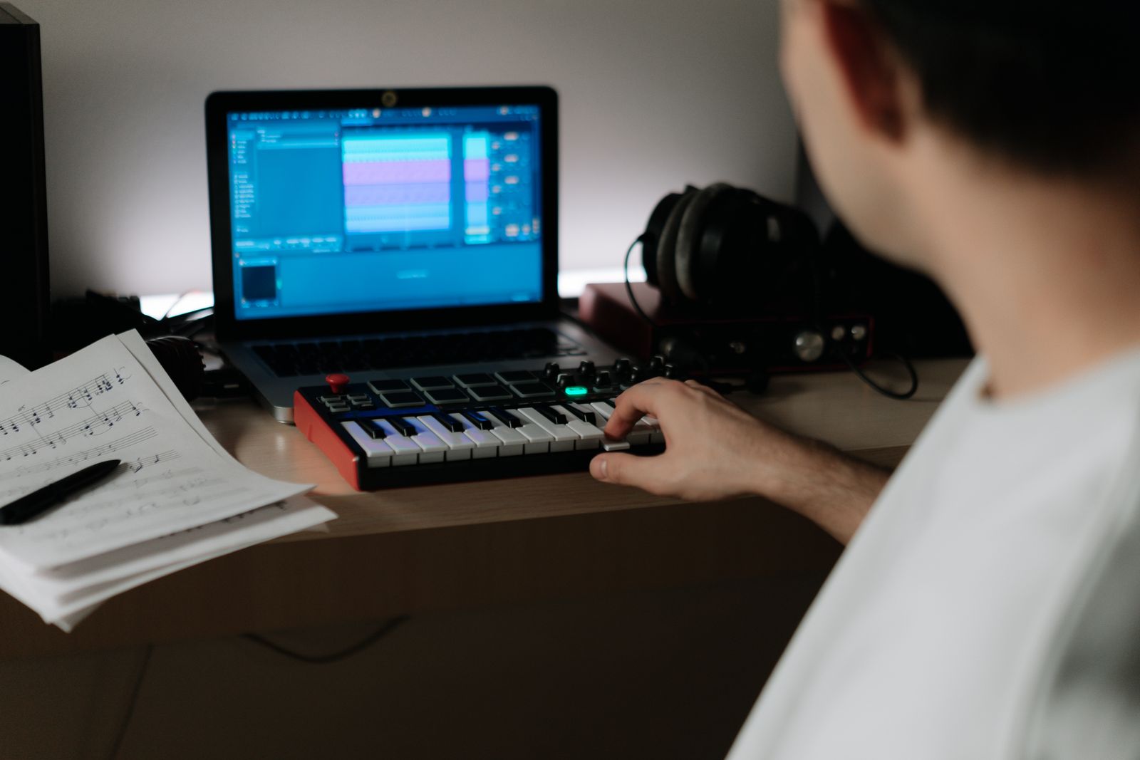 Musician playing a keyboard controller beside a laptop